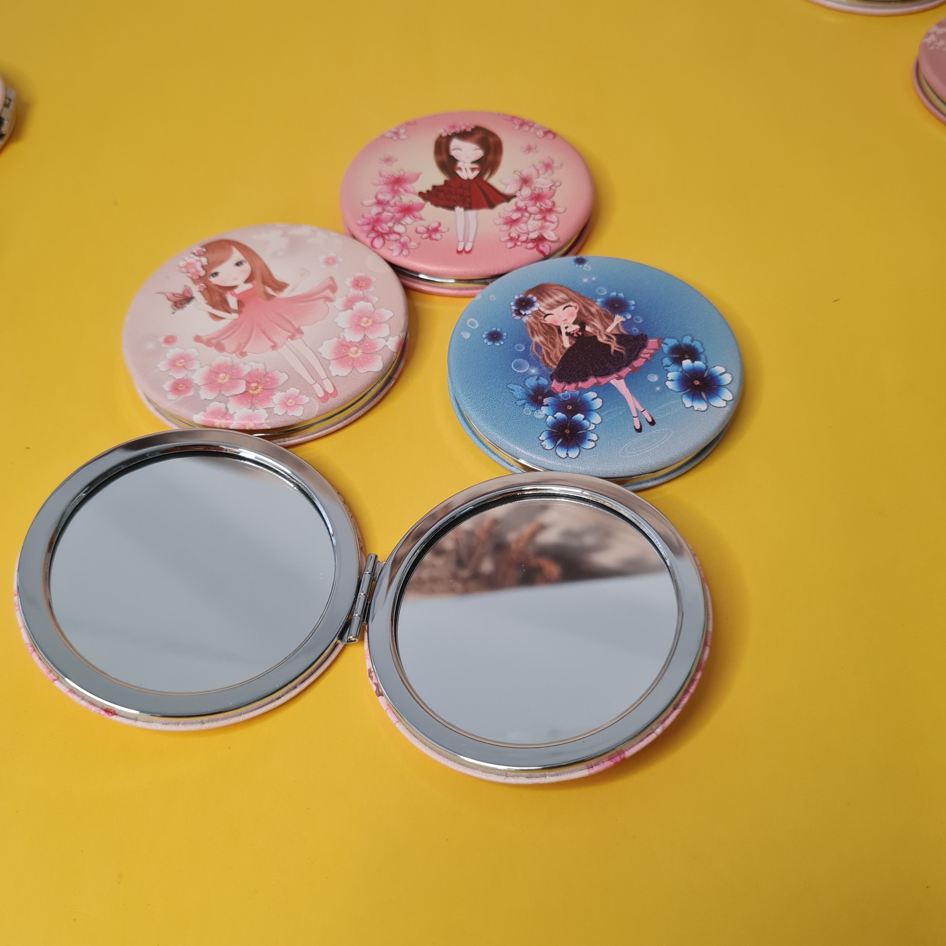 Compact mirrors with decorative cases on a yellow background